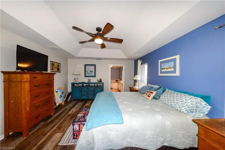 Primary Bedroom featuring a tray ceiling, luxury vinyl wood-type flooring, ceiling fan, and ensuite bath