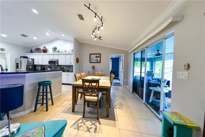 Tiled dining space with vaulted ceiling, rail lighting, and crown molding