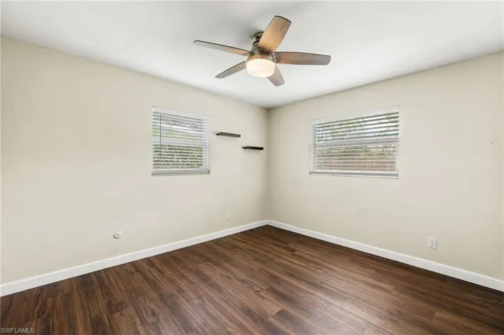 Empty room with dark hardwood / wood-style flooring, ceiling fan, and plenty of natural light