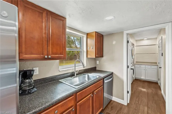 Kitchen featuring sink, stainless steel appliances, dark hardwood / wood-style floors, a textured ceiling, and stacked washer and clothes dryer