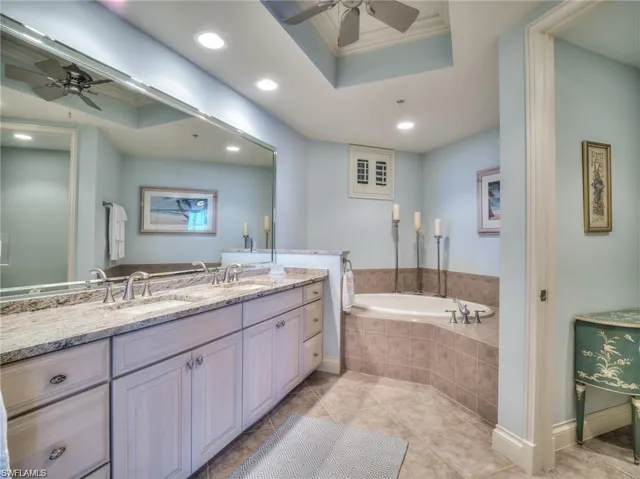 Bathroom featuring tile patterned floors, vanity, a raised ceiling, and tiled bath