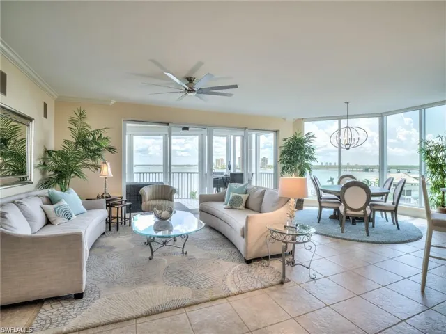 Tiled living room with ceiling fan with notable chandelier, a healthy amount of sunlight, a water view, and crown molding