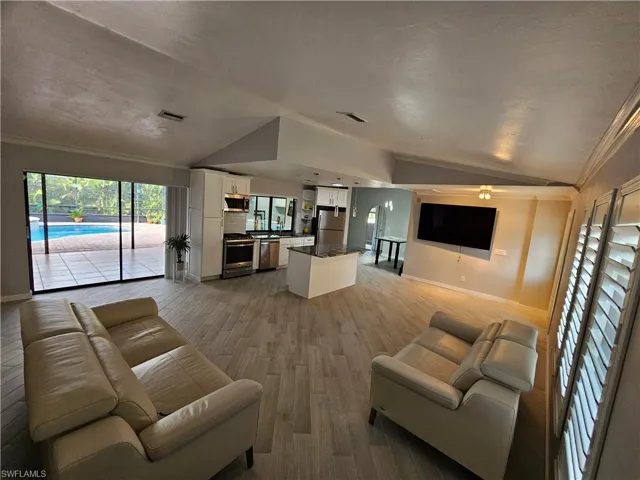 Living room with lofted ceiling, light wood finished floors, visible vents, and crown molding