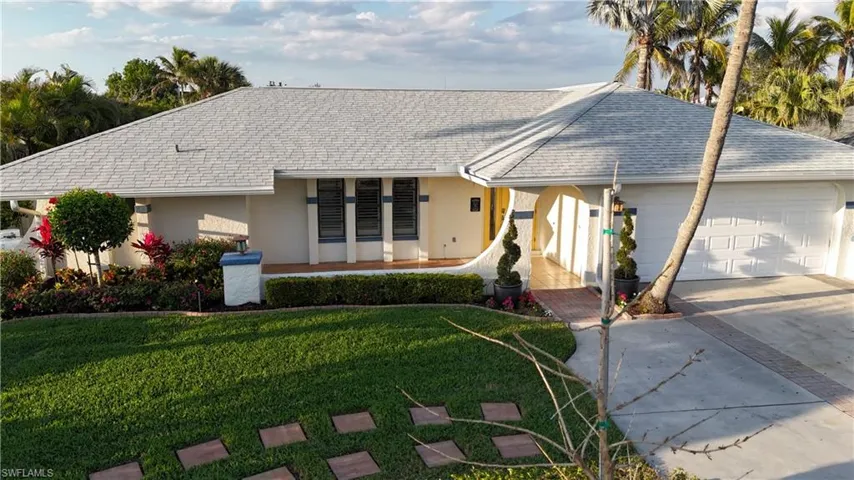 Ranch-style house with stucco siding, a shingled roof, a front yard, a garage, and driveway