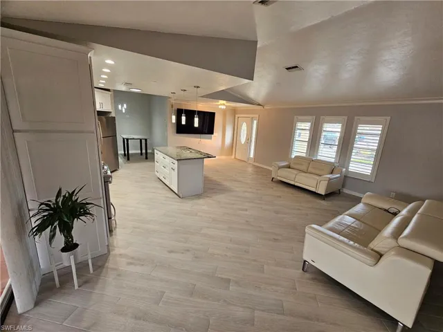 Living area with light wood finished floors, baseboards, visible vents, and crown molding
