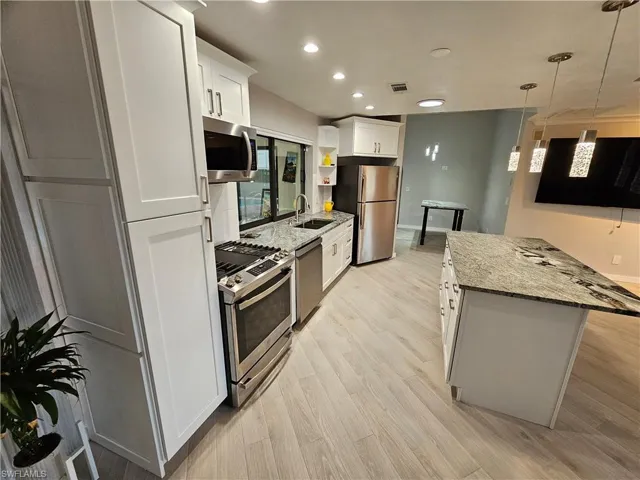 Kitchen with light stone counters, stainless steel appliances, a sink, white cabinetry, and light wood-style floors
