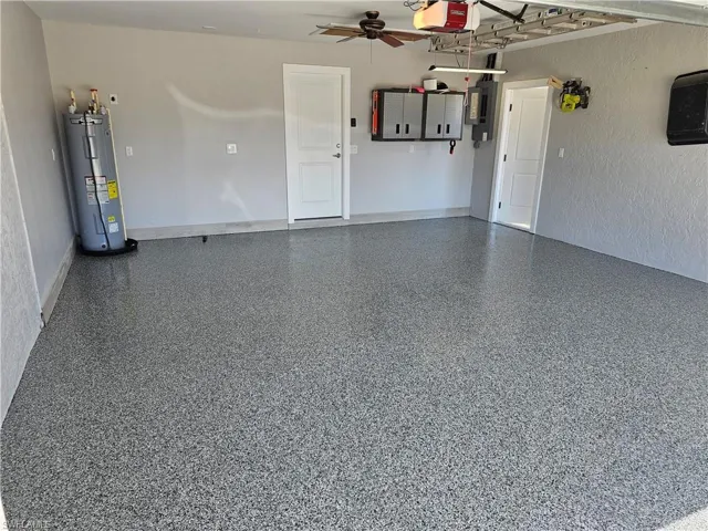 Garage featuring electric water heater, a ceiling fan, baseboards, electric panel, and a garage door opener