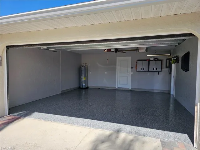 Garage with a garage door opener, electric water heater, baseboards, and a ceiling fan