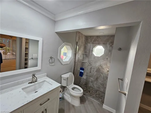 Bathroom with toilet, wood finished floors, vanity, a shower stall, and crown molding