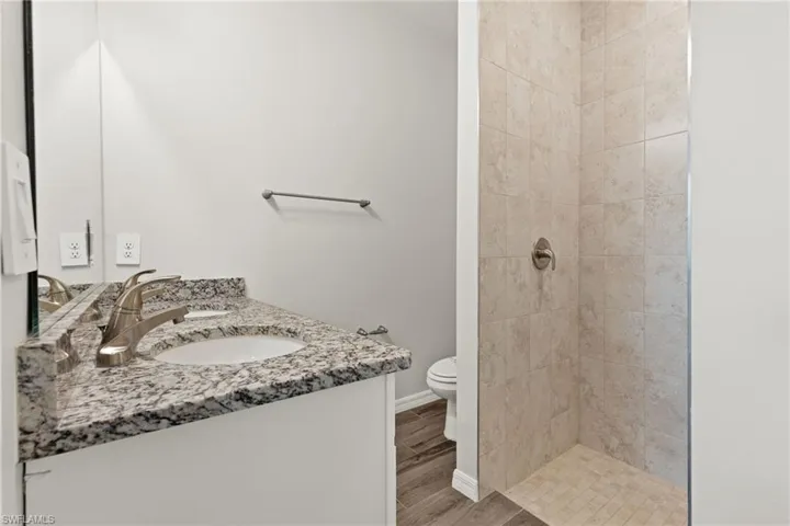 Bathroom with double vanity, a tile shower, wood-type flooring, and toilet