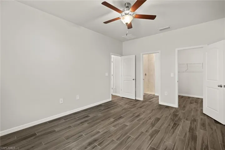 Unfurnished bedroom featuring a spacious closet, dark hardwood / wood-style floors, ceiling fan, and a closet