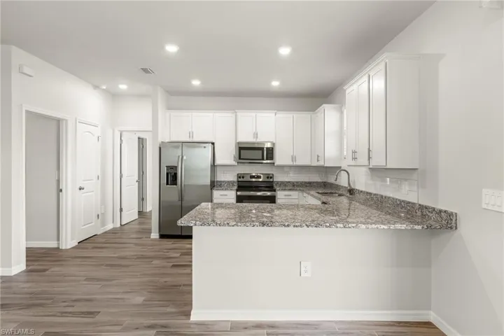 Kitchen featuring kitchen peninsula, light stone counters, stainless steel appliances, hardwood / wood-style flooring, and sink