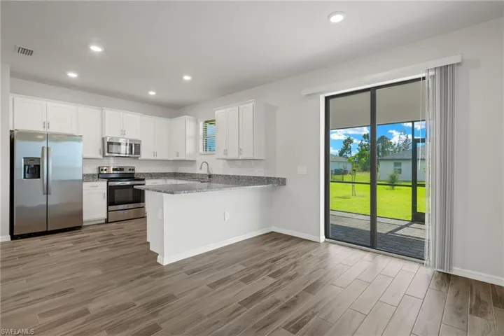 Kitchen with hardwood / wood-style flooring, stainless steel appliances, white cabinets, light stone countertops, and kitchen peninsula