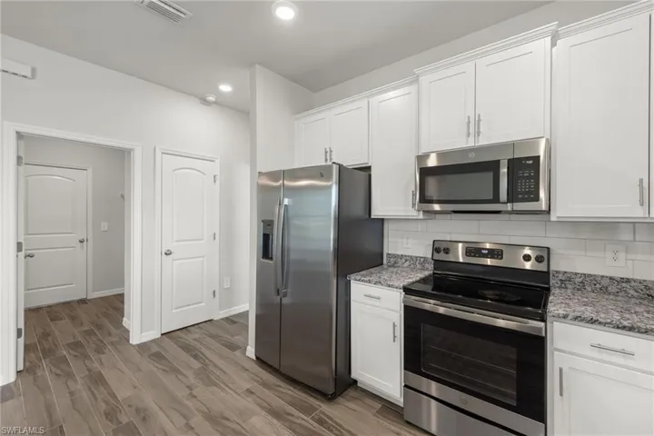 Kitchen featuring decorative backsplash, light hardwood / wood-style flooring, appliances with stainless steel finishes, and white cabinets