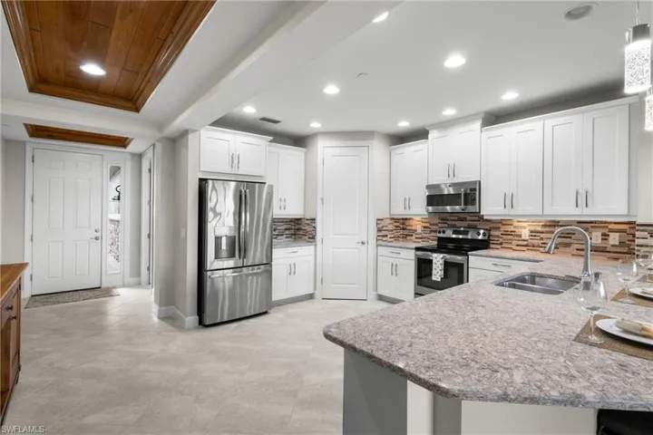 Kitchen featuring appliances with stainless steel finishes, light stone counters, white cabinetry, tasteful backsplash, and recessed lighting