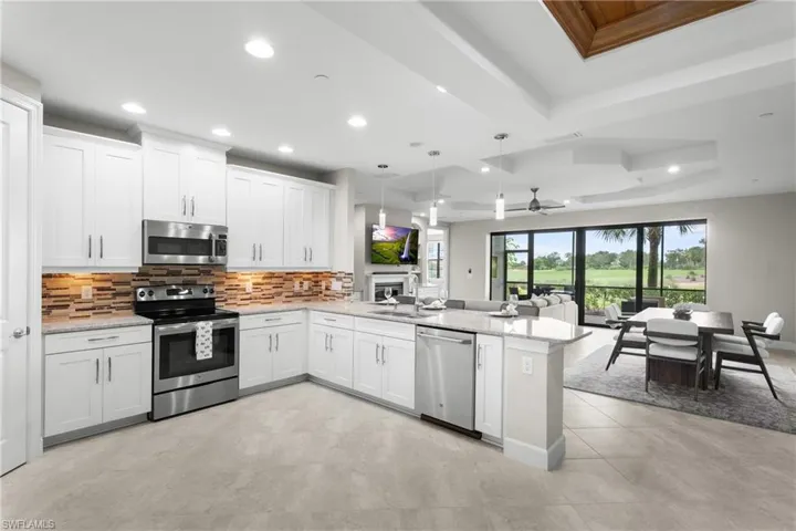 Kitchen with stainless steel appliances, a raised ceiling, open floor plan, a peninsula, and tasteful backsplash