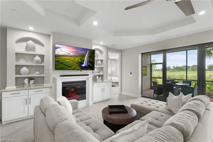 Living area with a raised ceiling, a ceiling fan, built in shelves, a glass covered fireplace, and recessed lighting
