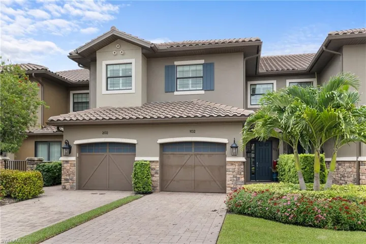 Multi unit property with stucco siding, stone siding, a tile roof, and driveway