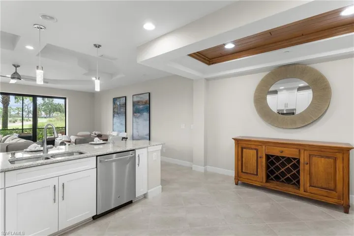 Kitchen with stainless steel dishwasher, a raised ceiling, light stone counters, hanging light fixtures, and open floor plan