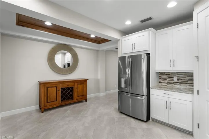 Kitchen featuring stainless steel refrigerator with ice dispenser, a tray ceiling, recessed lighting, tasteful backsplash, and white cabinetry