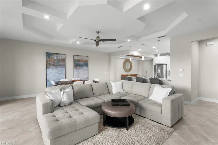 Living room with light tile patterned floors, ceiling fan, a tray ceiling, and recessed lighting