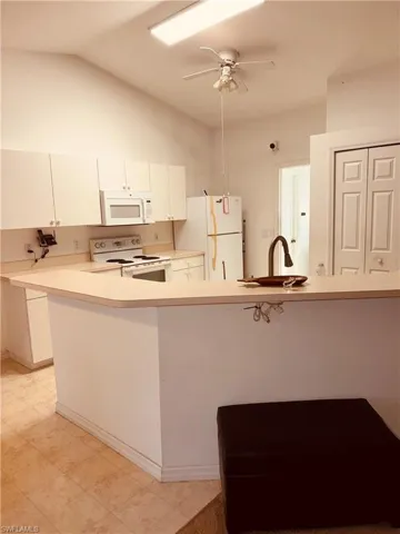 Kitchen with a peninsula, light countertops, white appliances, white cabinets, and ceiling fan