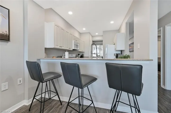 Kitchen featuring white appliances, kitchen peninsula, white cabinetry, dark wood-type flooring, and a breakfast bar