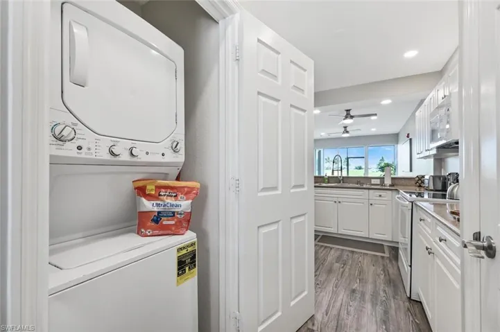 Clothes washing area featuring stacked washer and clothes dryer, wood-type flooring, sink, and ceiling fan