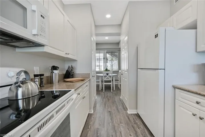 Kitchen with light hardwood / wood-style flooring, white cabinets, and white appliances