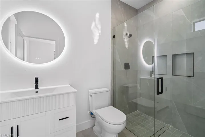 Bathroom with baseboards, toilet, vanity, and a stall shower