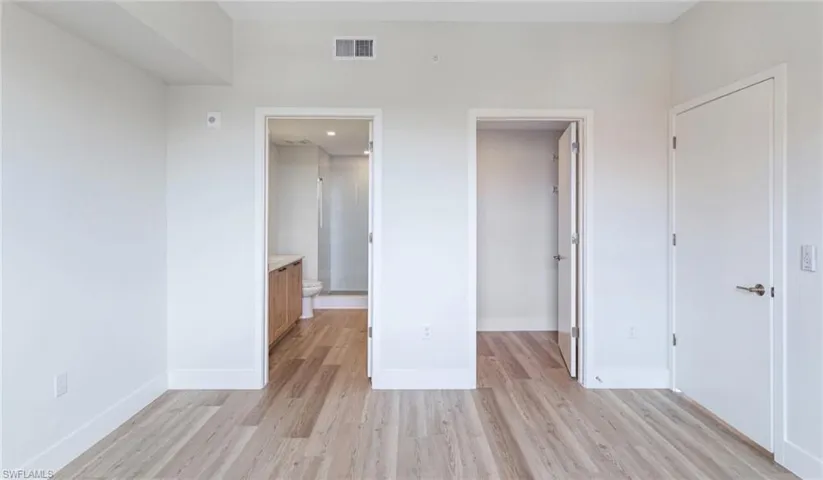 Unfurnished bedroom featuring a closet, baseboards, light wood-style flooring, a walk in closet, and visible vents