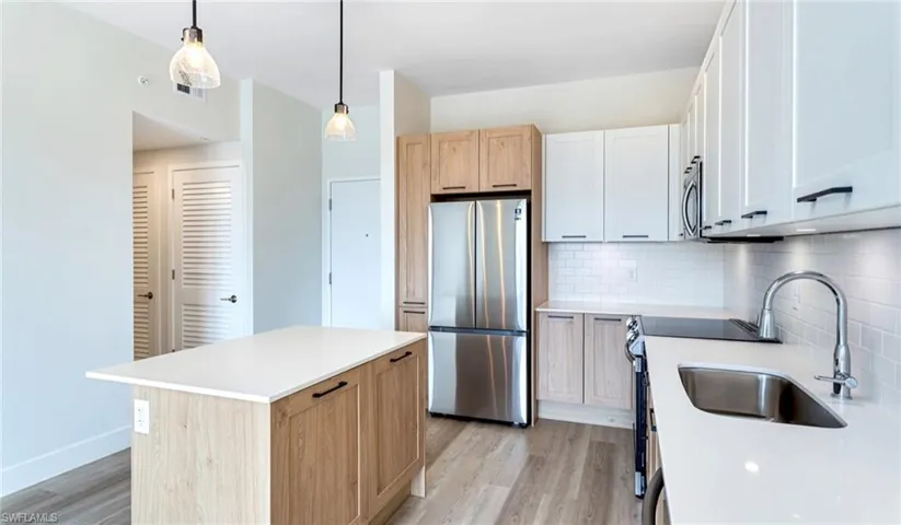Kitchen with appliances with stainless steel finishes, light wood finished floors, a sink, and backsplash