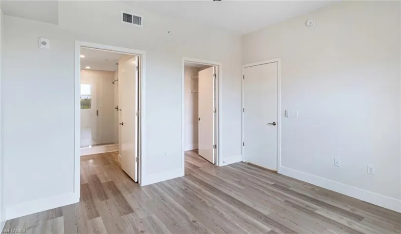 Unfurnished bedroom with a closet, visible vents, a walk in closet, light wood finished floors, and baseboards