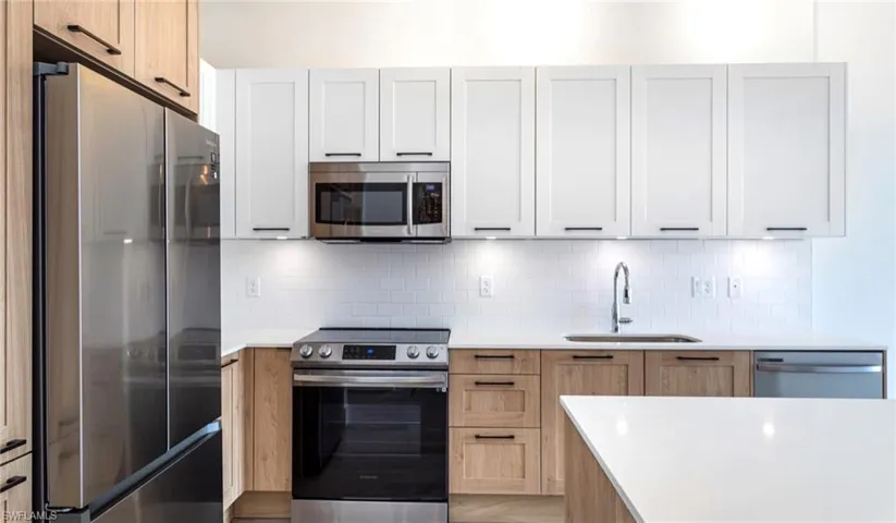 Kitchen with a sink, light countertops, white cabinetry, stainless steel appliances, and decorative backsplash
