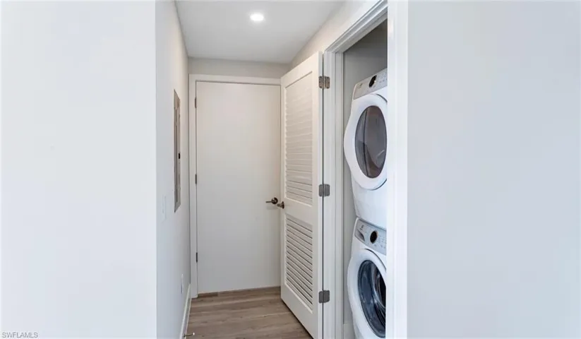 Clothes washing area featuring stacked washer / dryer, laundry area, light wood finished floors, and recessed lighting