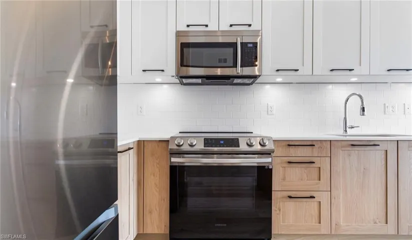 Kitchen with a sink, light countertops, white cabinetry, stainless steel appliances, and decorative backsplash