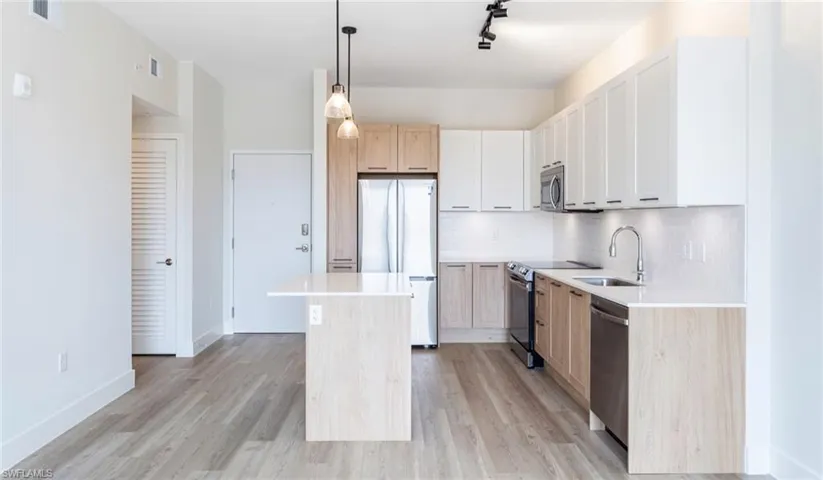 Kitchen featuring a sink, light countertops, light wood finished floors, stainless steel appliances, and backsplash