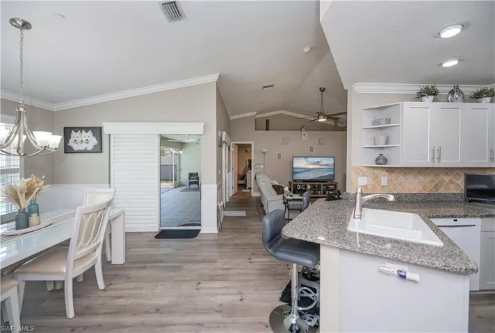 Kitchen with vaulted ceiling, ceiling fan with notable chandelier, tasteful backsplash, LVT plank wood style flooring