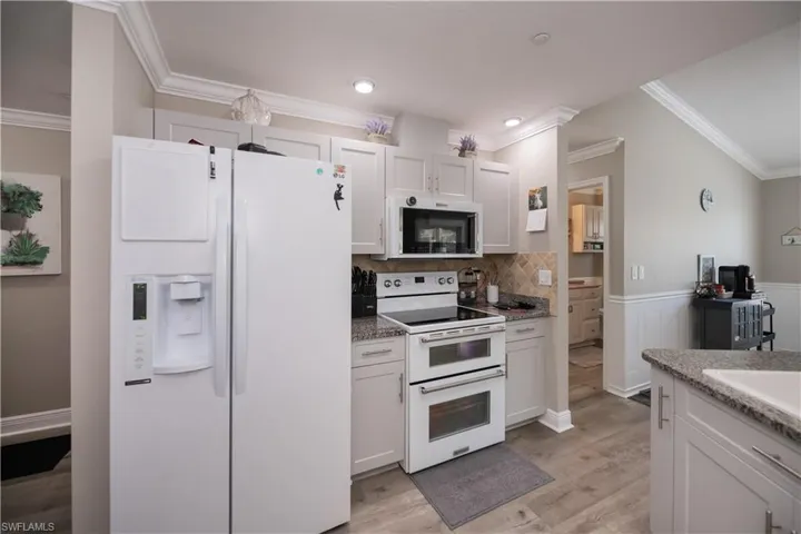 Kitchen with ornamental molding,  white appliances, white cabinets, granite countertops, and tasteful backsplash