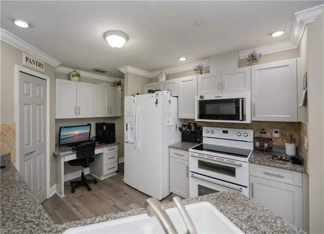 Kitchen with backsplash, crown molding, hardwood / white cabinets, granite countertops, and pantry