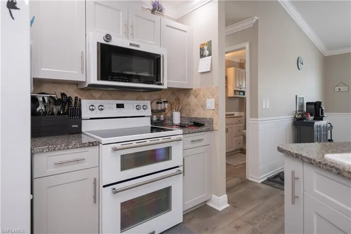 Kitchen featuring Kitchenaid range with two ovens, convection oven and mircrowave, backsplash, white cabinetry, granite countertops, and ornamental crown molding