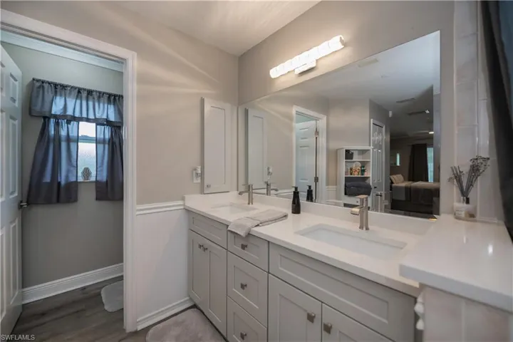 Bathroom featuring dual sinks, vanity with extensive cabinet space, water closet, and LVT plank wood-style flooring