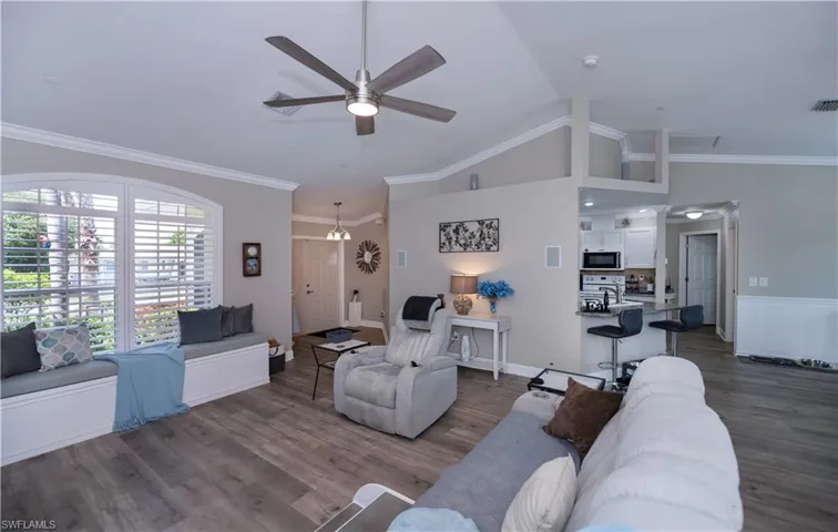Living room with crown molding, high vaulted ceiling, ceiling fan, LVT wood plank style flooring