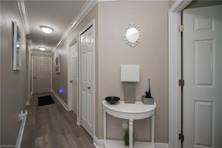 Hallway featuring LVT plank wood-style floors and crown molding, leads to guest bedrooms, laundry room & garage