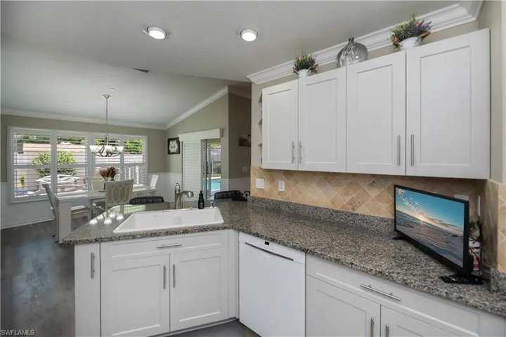 Kitchen with crown molding, LVT plank wood-style floors, backsplash, granite countertops, and dishwasher