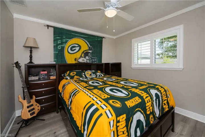 Bedroom with LVT plank wood-style floors, ceiling fan, plantation shutters, and crown molding