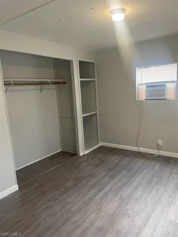 Unfurnished bedroom featuring cooling unit, dark wood-type flooring, and a closet