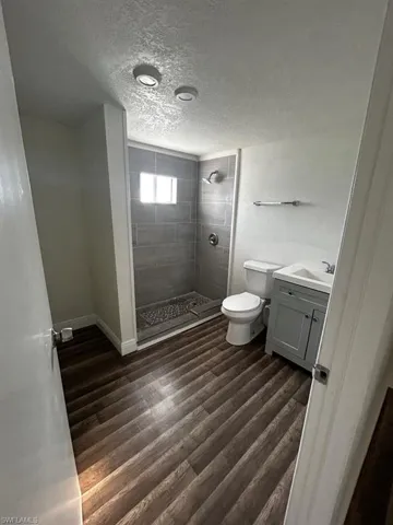 Bathroom with hardwood / wood-style flooring, vanity, a tile shower, a textured ceiling, and toilet