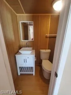 Bathroom with toilet, hardwood / wood-style floors, vanity, and wood walls