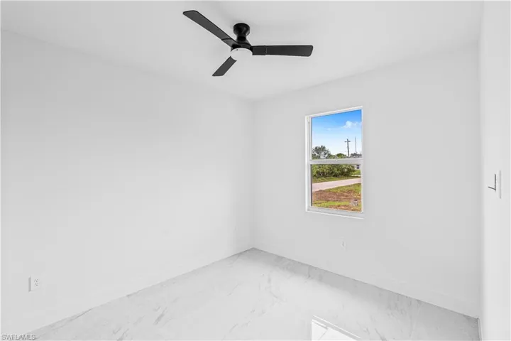 Room featuring large-format light-toned stone-finish flooring, matte black three-blade ceiling fan, and single-pane window